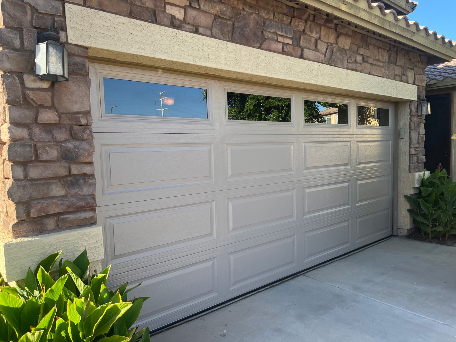 Tan raised panel garage door with windows on stone-front Phoenix home